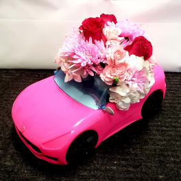Pink toy car topped with a bouquet of red, pink, and white flowers