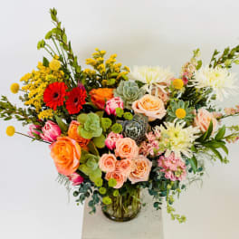 Mixed bouquet of roses, gerbera daisies, and succulents in a glass vase
