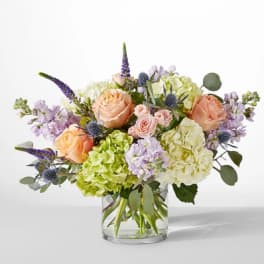 Peach roses and hydrangeas in a clear glass vase with lavender accents