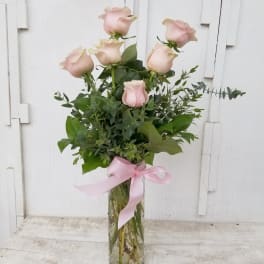 Tall bouquet of pale pink roses in a glass vase with a pink ribbon