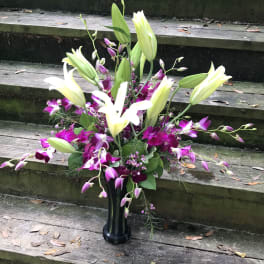 Tall floral arrangement with white lilies and purple orchids in a black vase