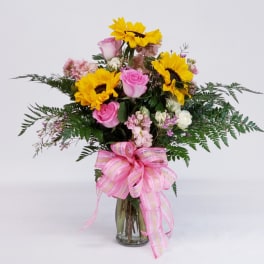 Bouquet of sunflowers and pink roses in a glass vase with a pink ribbon