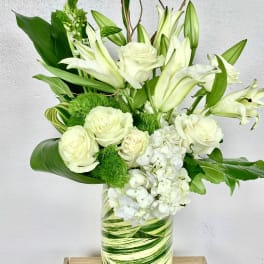 White roses and lilies arranged in a green-striped glass vase