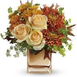 Cream roses and orange chrysanthemums in a clear vase