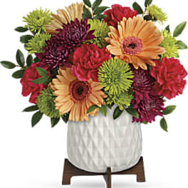 Colorful mixed flower arrangement in a white vase on a wooden stand