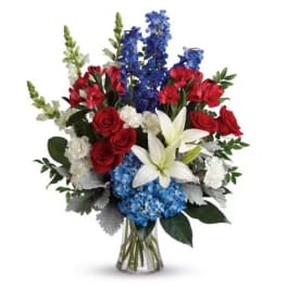 Bouquet of red roses, blue flowers, and white lilies in a clear vase