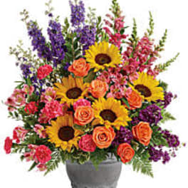 Mixed bouquet with sunflowers, orange roses, and purple flowers in a gray vase