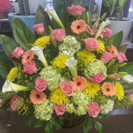 Large mixed bouquet with pink roses, white calla lilies, and yellow flowers in a basket