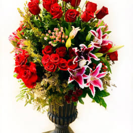 Tall arrangement of red roses and pink lilies in a dark pedestal vase