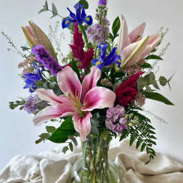 Mixed bouquet with pink lilies, blue irises, and purple flowers in a glass vase