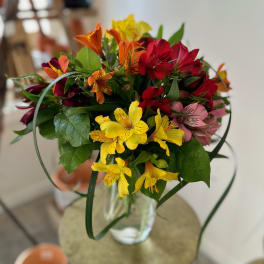 Mixed bouquet of red, yellow, orange, and pink flowers in a clear glass vase