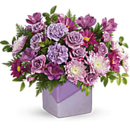 Purple mixed flower arrangement in a lavender square vase