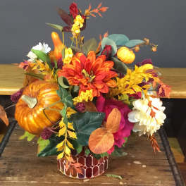 Autumn floral arrangement with pumpkins in a patterned container