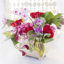 Mixed bouquet of red roses, pink orchids, and calla lilies in a white vase