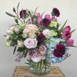 Mixed bouquet of pink, blue, and purple flowers in a clear glass vase