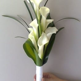 Hand-tied bouquet of white calla lilies with long linear foliage, wrapped in white ribbon.