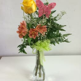 Yellow rose and orange flowers in a clear glass vase with a pink butterfly pick