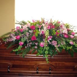 Pink and green casket spray arranged on a polished wooden casket
