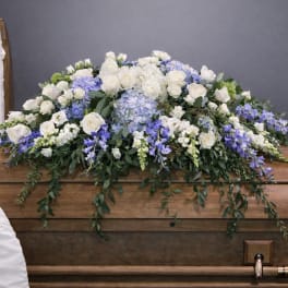 White and blue floral casket spray on a wooden casket