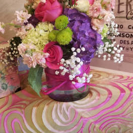 Pink, purple, and white flower arrangement in a round vase with a pink ribbon