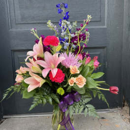 Mixed bouquet of pink lilies, roses, and purple flowers in a glass vase