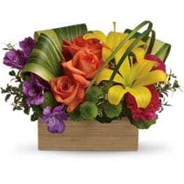 Colorful bouquet of roses, lilies, and purple flowers in a wooden box