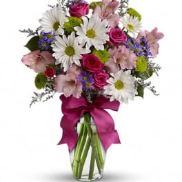 Bouquet of daisies, pink roses, and lilies in a glass vase with a magenta ribbon