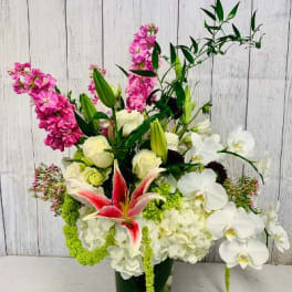 Tall mixed bouquet with white orchids, lilies, hydrangeas, and pink flowers in a glass vase