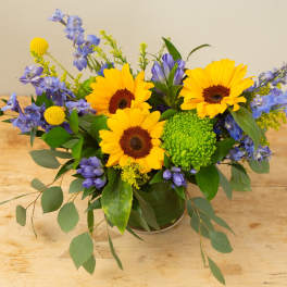 Sunflowers and blue flowers arranged in a low vase