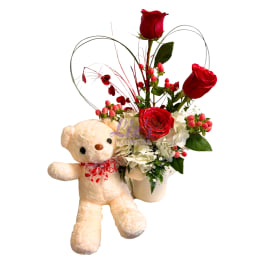 Red roses in a white vase with a teddy bear