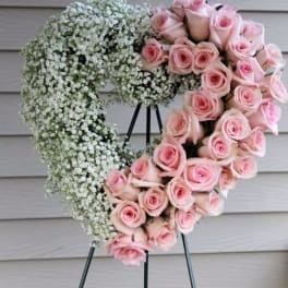 Heart-shaped standing wreath with pink roses and white filler flowers on a metal easel