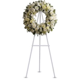 White floral wreath of roses, lilies, and mums displayed on a tall white metal easel