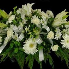 White floral casket spray with lilies, daisies, and ribbon accents