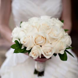 Hand-tied bouquet of ivory roses held by a person in a white strapless dress