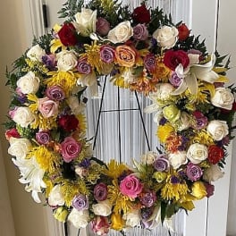 Large circular standing wreath of mixed roses, lilies, and yellow mums on a metal easel stand