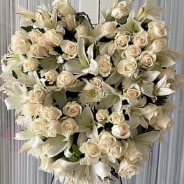 Heart-shaped standing spray of ivory roses and white lilies on a metal easel