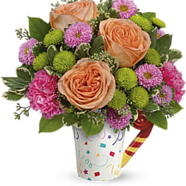 Peach roses and pink flowers in a confetti-patterned cup with a candy cane pick