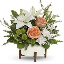 White lilies and peach roses in a white container with green accents