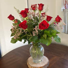 Red roses arranged in a clear glass vase on a wood slice base