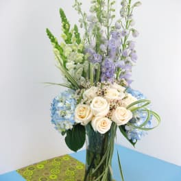Blue hydrangeas and cream roses in a tall glass vase with lavender spikes