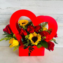 Red heart-shaped box filled with roses, sunflowers, and carnations