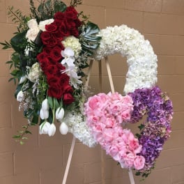 Heart-shaped floral wreath on an easel with red, white, pink, and purple flowers