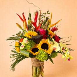 Tropical bouquet with sunflowers, orchids, and red heliconia in a glass vase