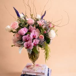 Mixed bouquet of pink roses, orchids, and white blooms in a glass vase