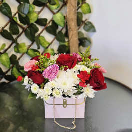 Mixed bouquet of red roses, white daisies, and pink carnations in a pink box