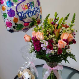 Birthday balloon beside a mixed flower bouquet in a glass vase and a small gift bag