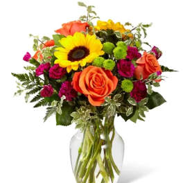 Bouquet of orange roses, yellow sunflowers, and magenta flowers in a glass vase