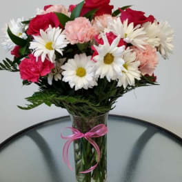 Bouquet of red roses, pink carnations, and white daisies in a glass vase