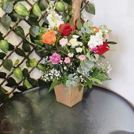 Mixed bouquet of roses, carnations, and white filler flowers in a paper box