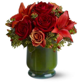 Compact arrangement of red roses and orange lilies in a green glass vase